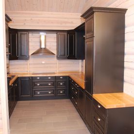 Et sort kjøkken med naturtre som kjøkkenbenkeplate med lyse furuvegger i rommet