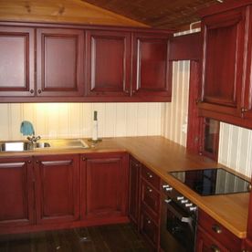 Et furukjøkken med rødmalte dører, naturtre som kjøkkenbenk og moderne inventar 