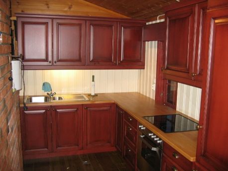 Et furukjøkken med rødmalte dører, naturtre som kjøkkenbenk og moderne inventar 