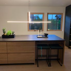 Moderne kjøkken med en kjøkkenøy med skap i eik og en benkeplate som er svart i et stilrent rom med matchende kjøkken, bar stoler og hyller og skap