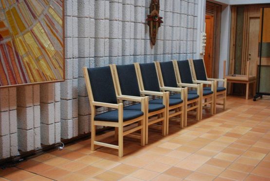 Stoler av lyst tre med rygg og sete av stoff plassert i en rad inne i en bygning