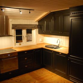 Et sort kjøkken i et rom med delvis skrått tak. Kjøkkenbenkeplaten er i naturtre