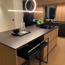 Moderne kjøkken med en kjøkkenøy med skap i eik og en benkeplate som er svart i et stilrent rom med matchende kjøkken, bar stoler og hyller og skap