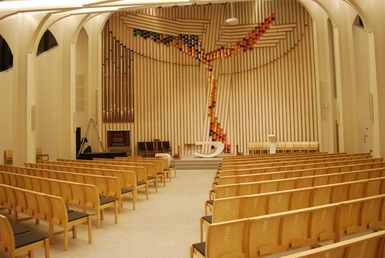 Innsiden av Hønefoss kirke med finera stoler som står på rad og rekke