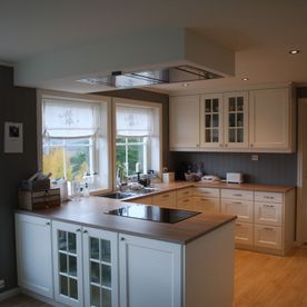 Et hvitt kjøkken i med mørke vegger og naturtre kjøkkenbenkeplate i en åpen romløsning