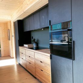 Moderne kjøkken med benkeplate og skap i lys eik og sort inventar, overhengsskap, stående skap og bakvegg i en sort matt farge