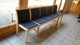 Finera stoler av lyst tre og blått stoff på rygg og sete som ersatt opp som en benk mot et vindu 