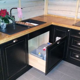 Et kjøkken med sorte dører på skaper og skuffer med moderne sort kjøkkenvask og kokeplate med en kjøkkenbenk i natur tre