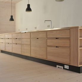 Lyst og moderne kjøkken i hvit eik med sorte detaljer på i et lyst rom med store vindu som slipper inn mye lys 