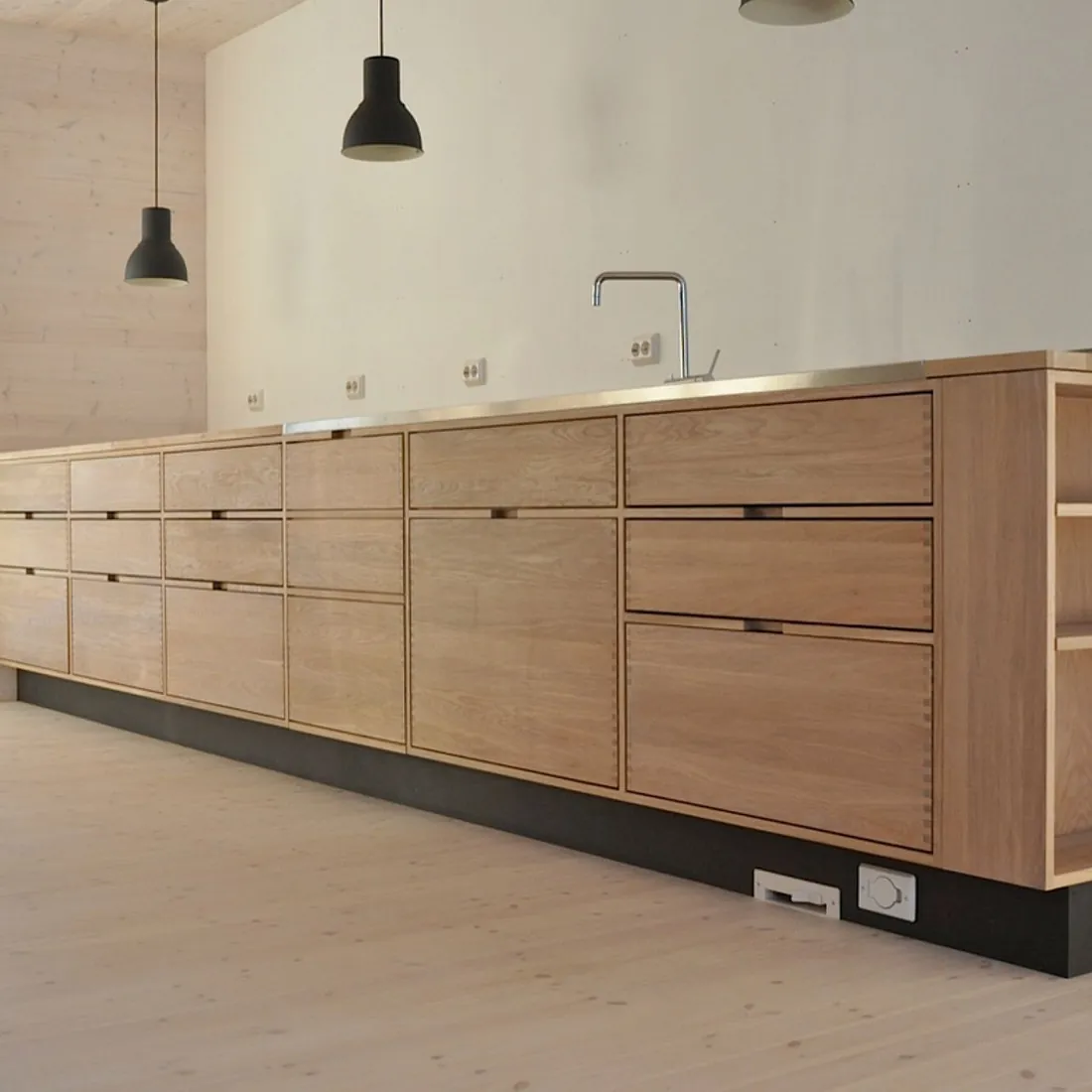 Lyst og moderne kjøkken i hvit eik med sorte detaljer på i et lyst rom med store vindu som slipper inn mye lys 